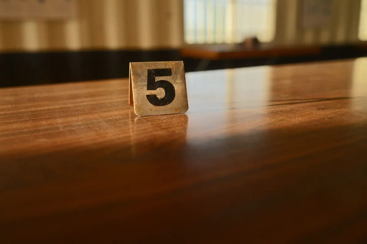 A small folded metal table card with a table number stands on a polished wooden table.