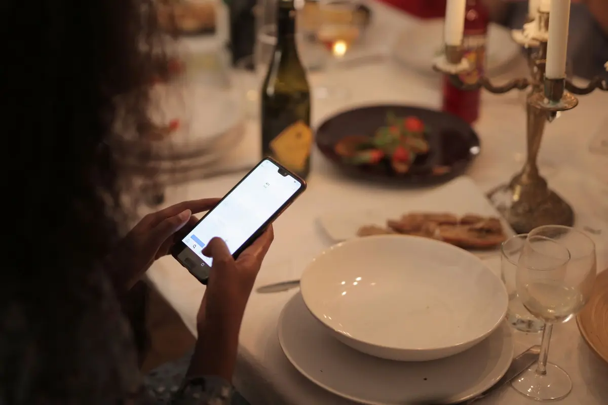 Two hands scroll a phone at a dinner table lit by candles.
