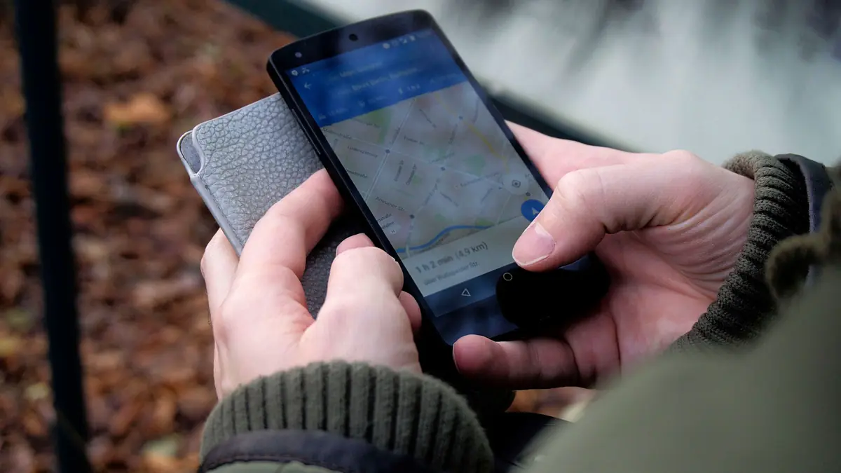 Two hands hold a smartphone showing a street map with a blue route line and a travel time.