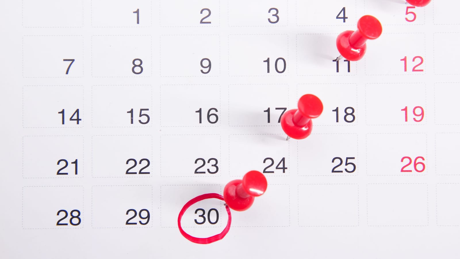 A paper calendar page with red push pins in several dates and one date circled in red.