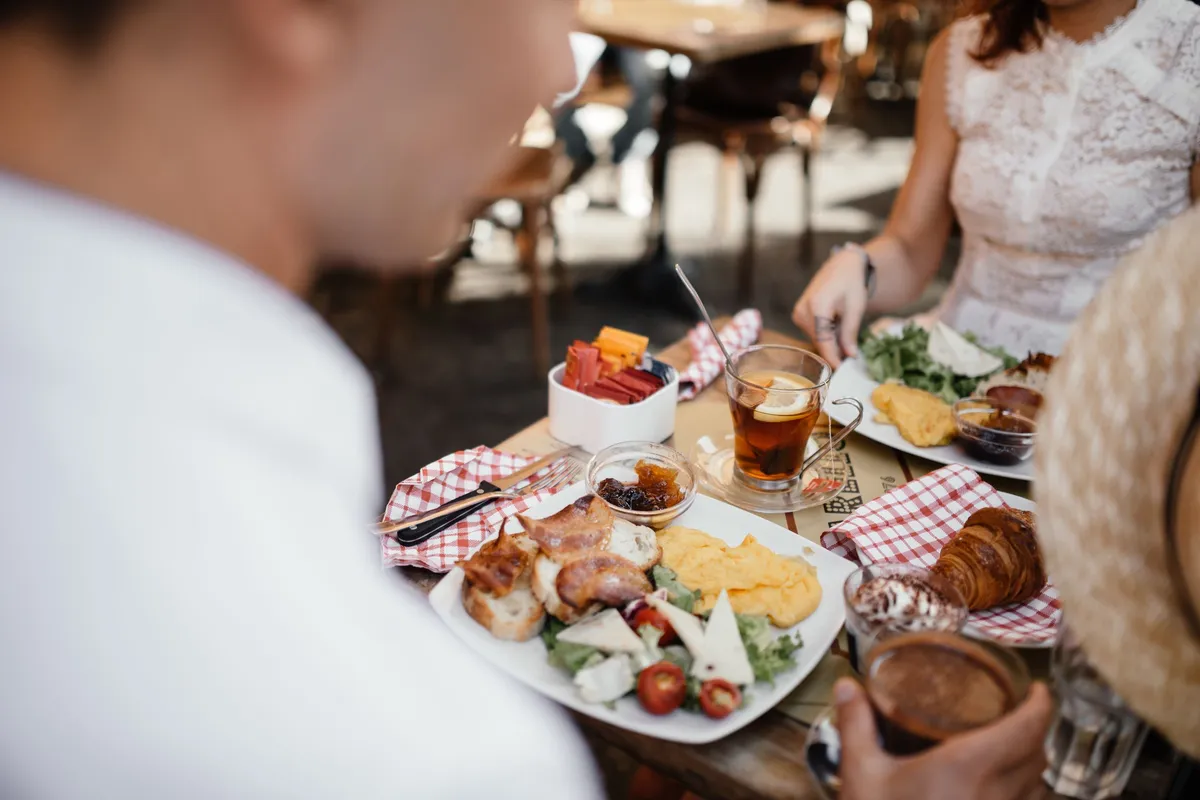 Friends share a brunch of eggs, salad and a croissant with tea at an outdoor café table.