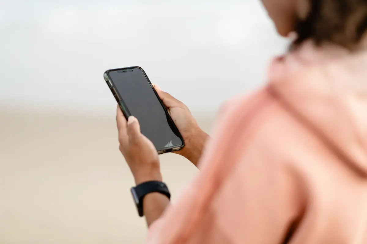 A person in a pink jacket holds a phone and looks at its screen.