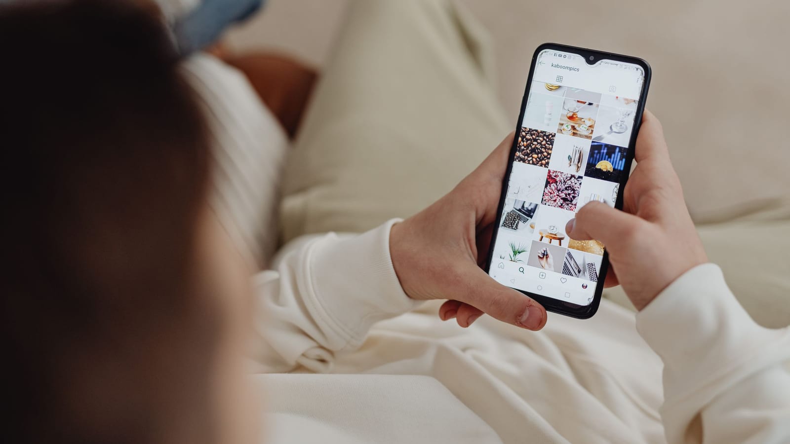 Hands holding a phone open on a grid of small photos in a social feed, a few of them food.