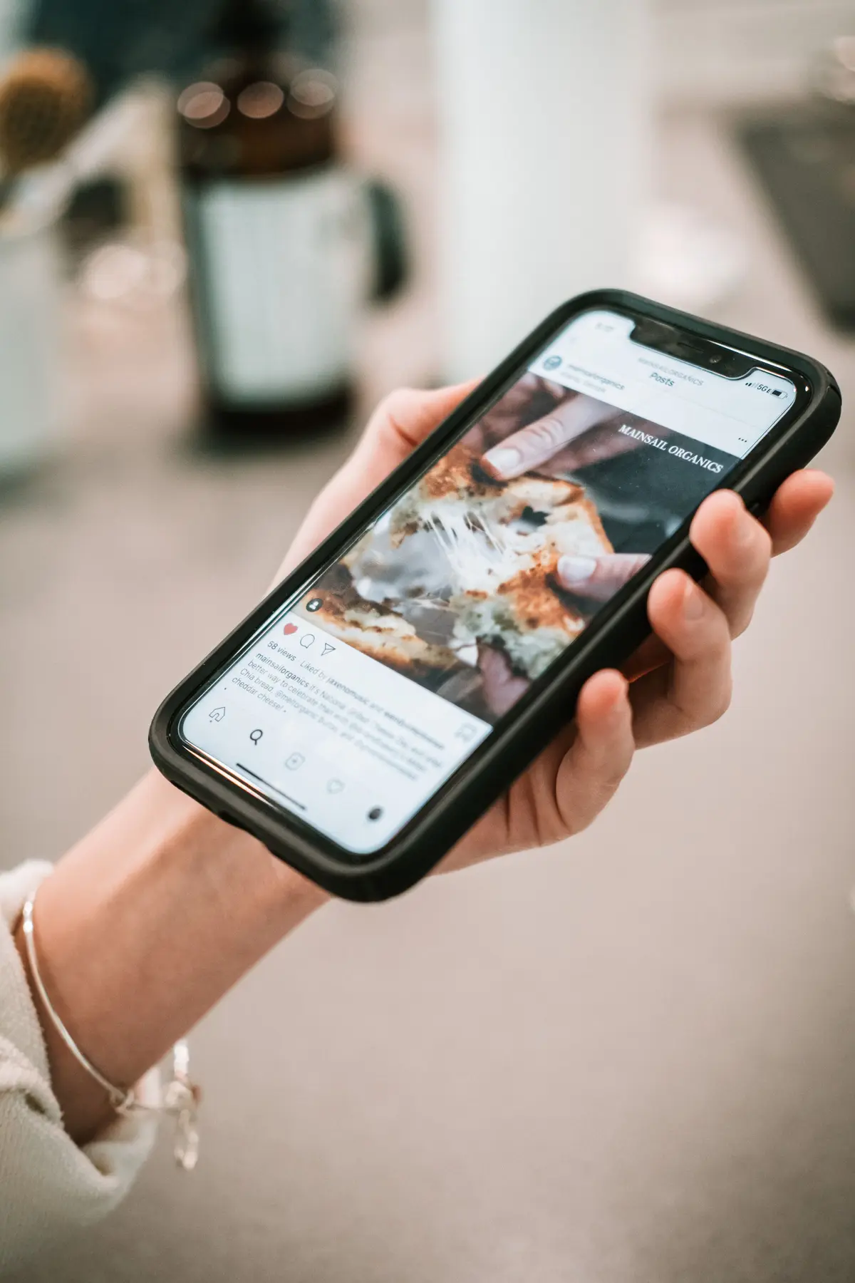 A hand holds a phone playing a food video of melting cheese, the room behind it out of focus.
