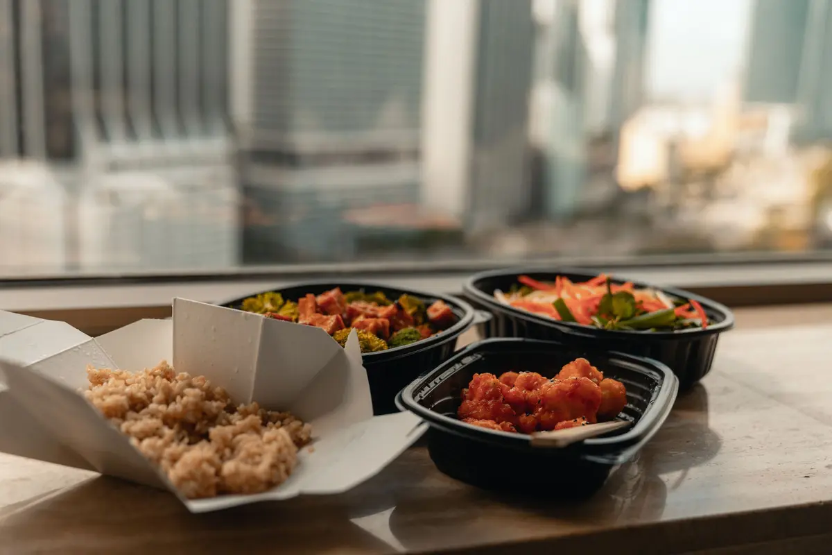 An open box of rice and three takeout containers of food sit on a stone window ledge.