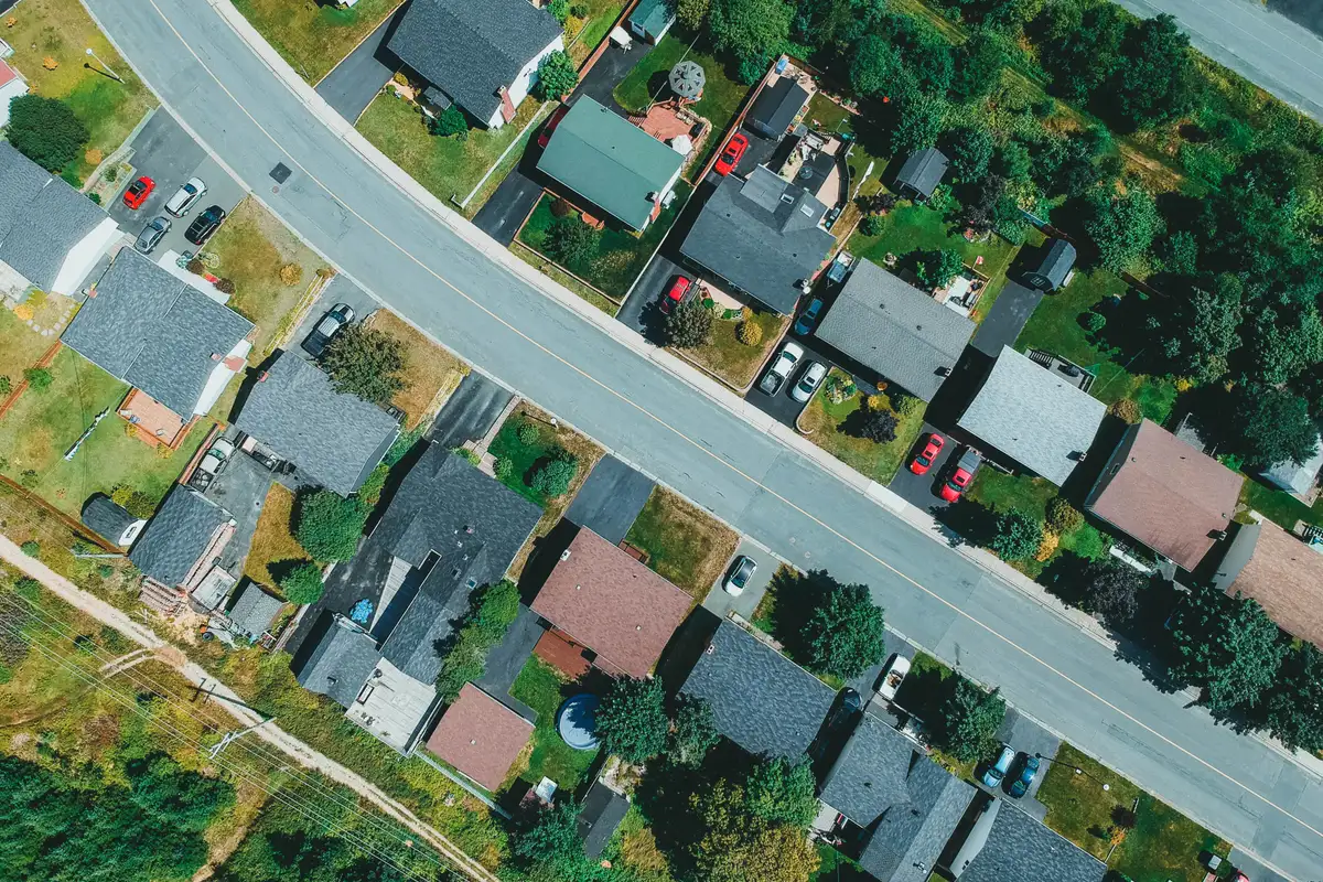 An aerial view of a suburban road lined with houses and trees.