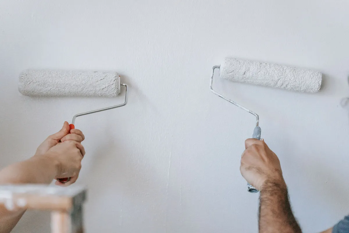 Two hands roll white paint onto a bare wall, the kind of build progress worth posting before opening.