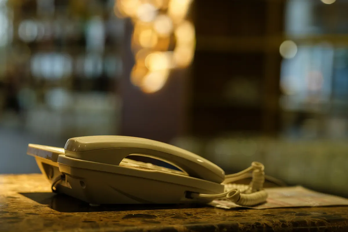 A landline phone sits on a restaurant bar counter, with shelves of bottles and warm lights blurred behind it.