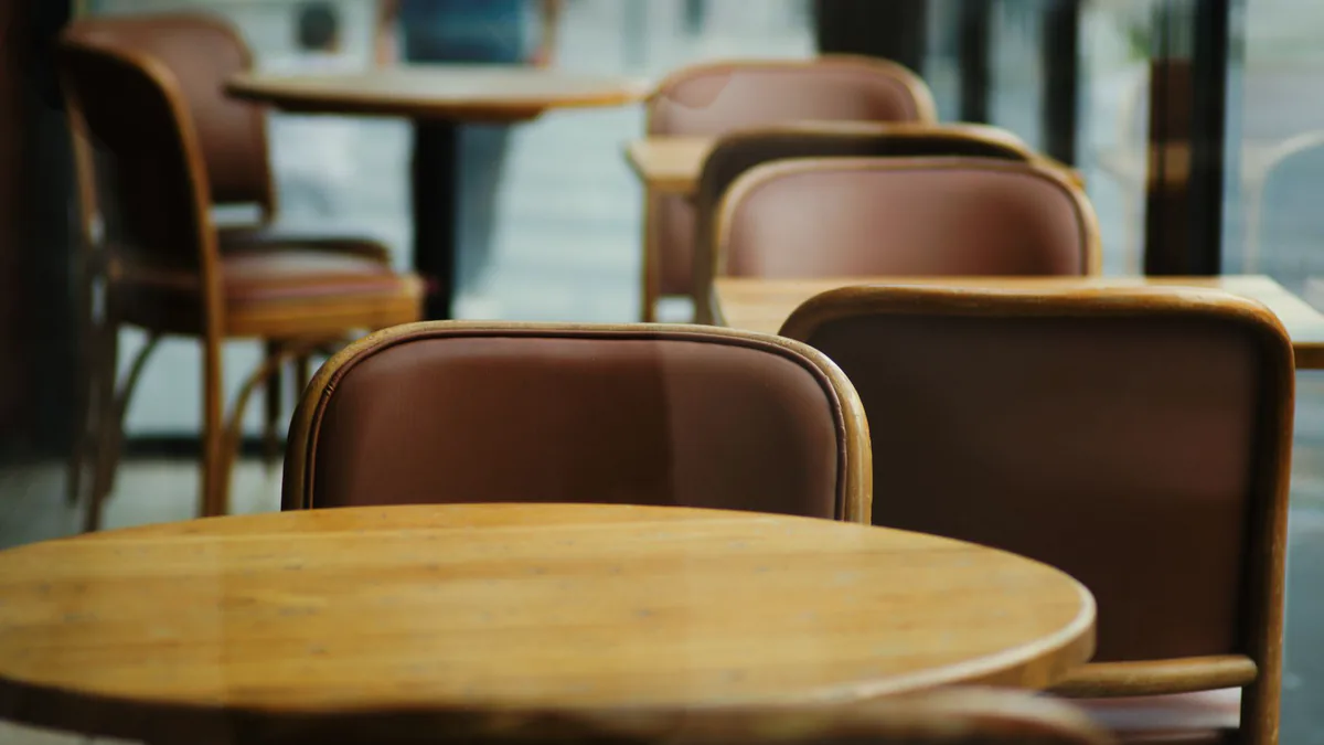 Empty round wooden tables and brown leather chairs in a quiet cafe, pale window light behind them