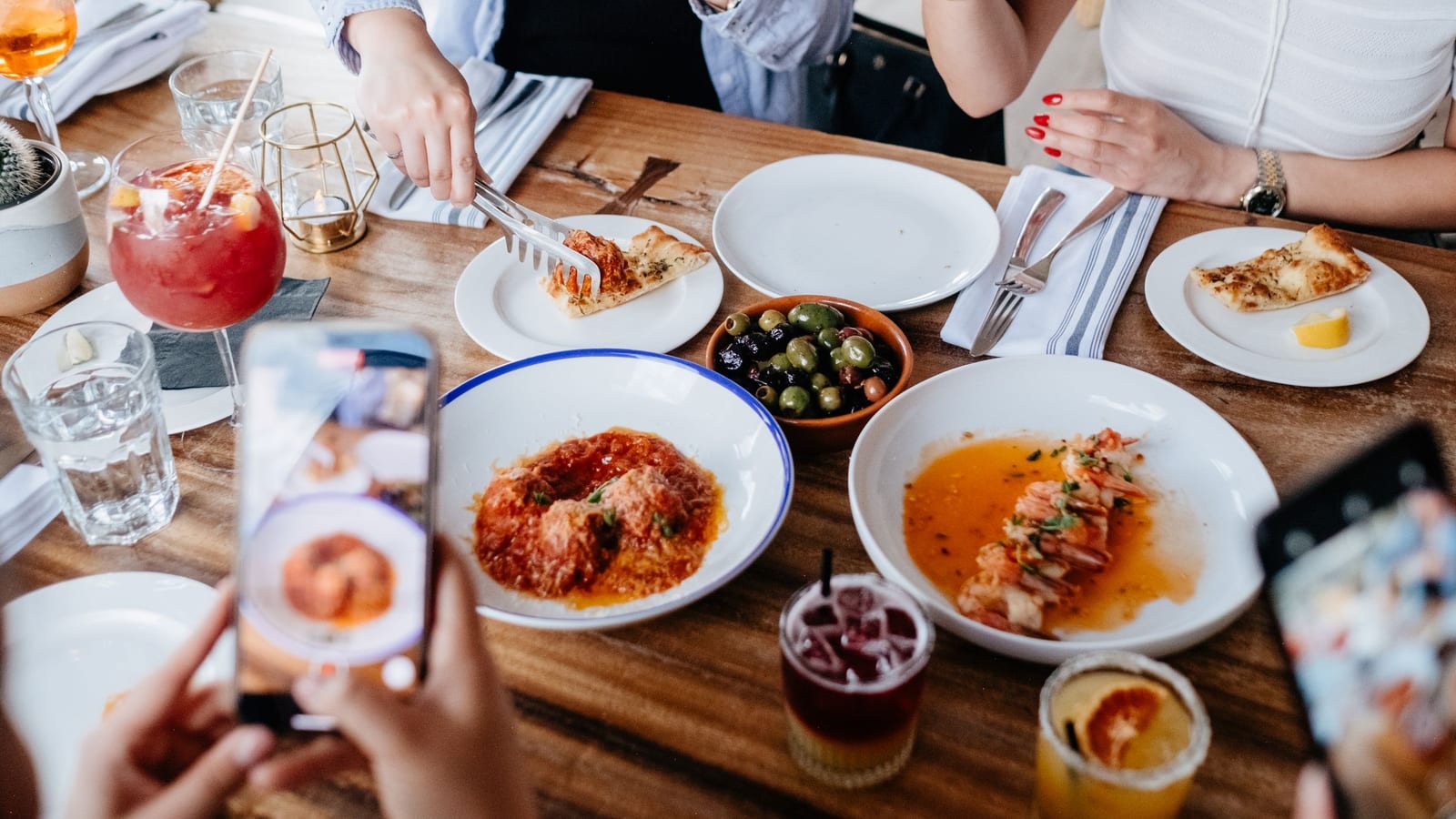Diners at a local restaurant table hold up their phones to photograph plates of food before they eat.