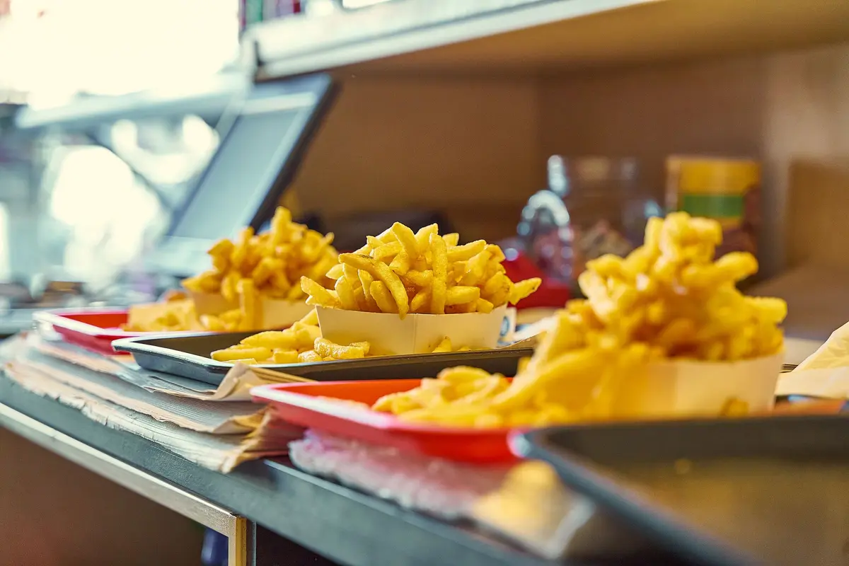 Paper boats of fries on red and grey trays line a restaurant counter beside the register, orders lined up for the lunch rush.