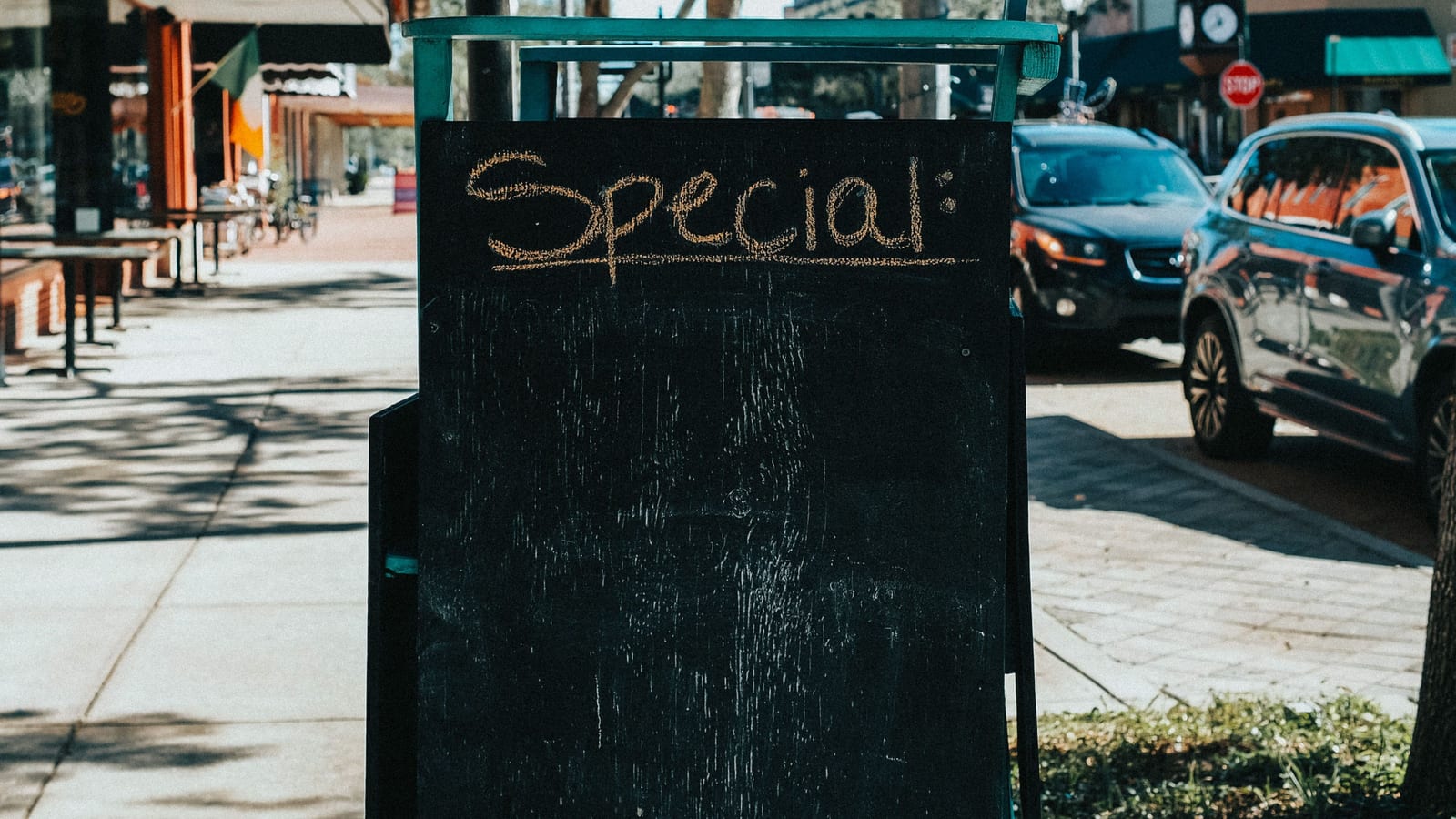 A chalkboard headed “Special:” on a small-town sidewalk beside outdoor tables, local store marketing at its simplest.