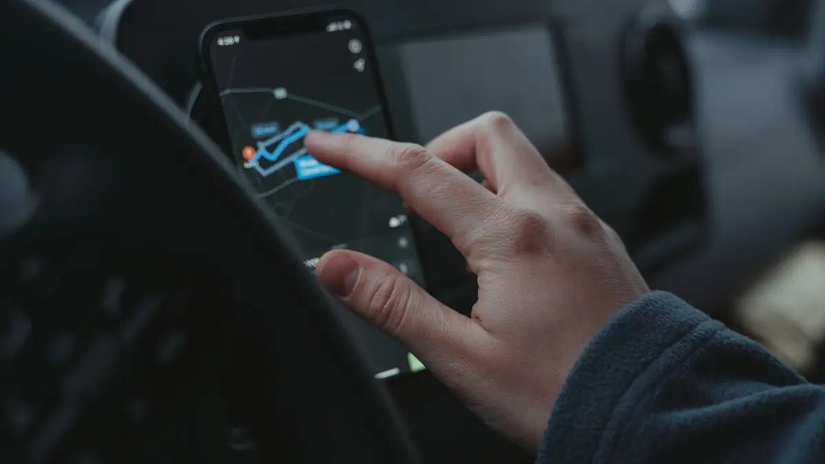 A hand taps a route on a phone mounted on a car dashboard.
